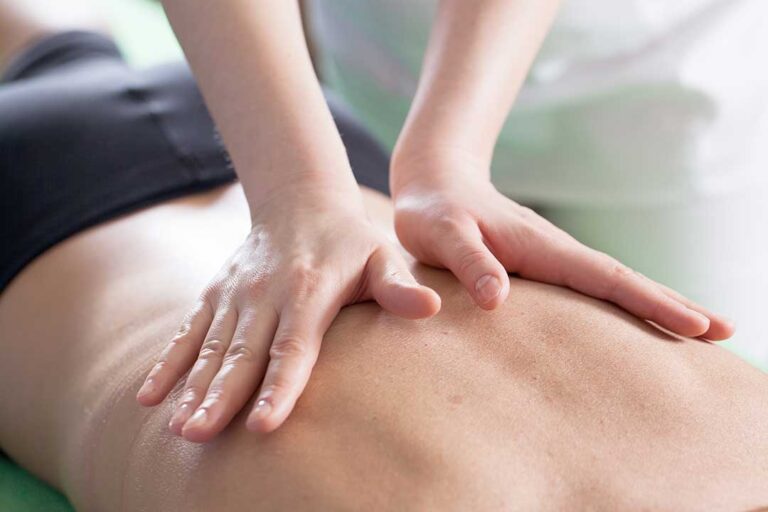 A clinician evaluates a standing patient’s spinal alignment beside a posture chart.